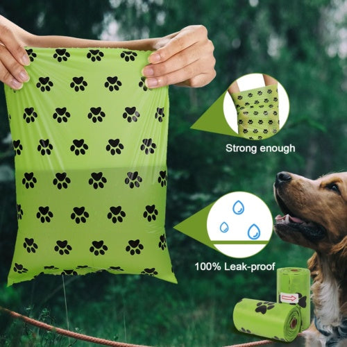 Green dog waste bags with paw pattern held by a hand, shown with a dog in the background.