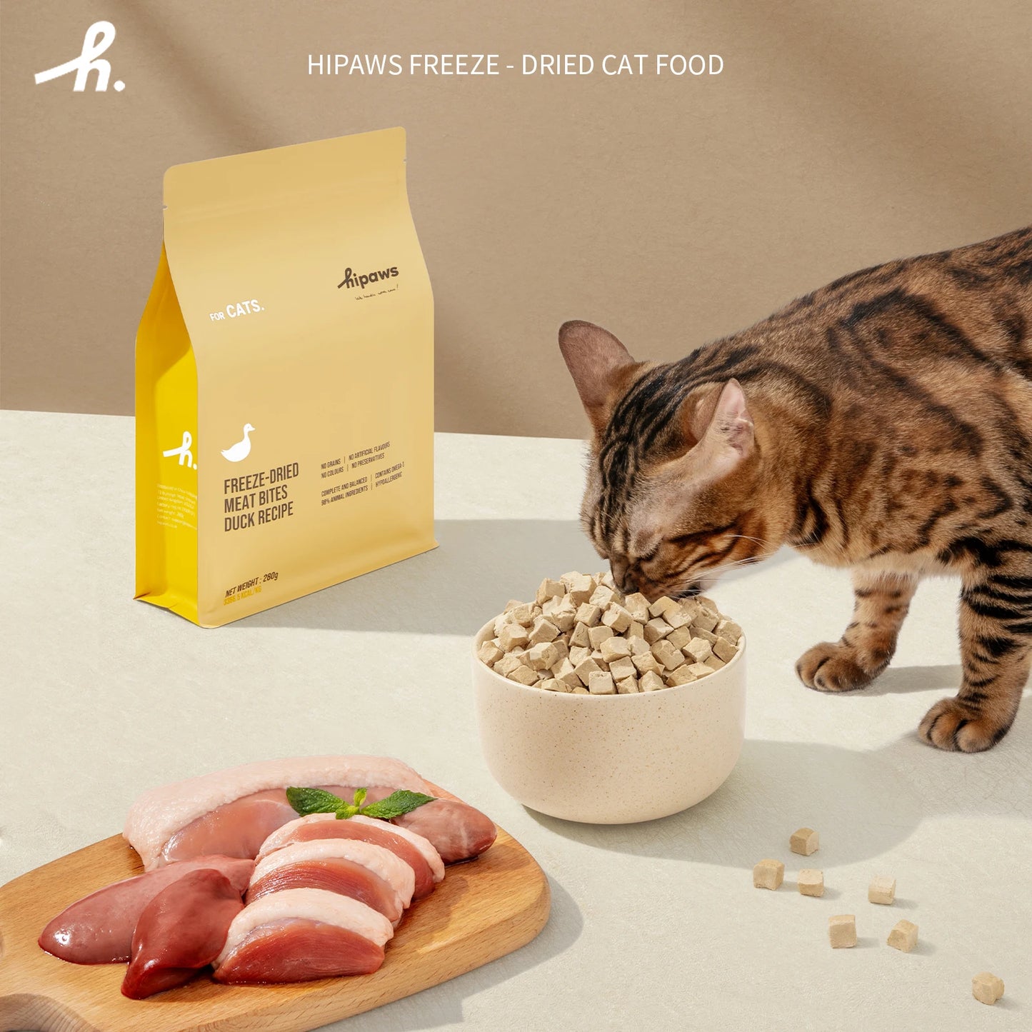 Cat eating from a bowl of freeze-dried cat food with a package labeled 'Hipaws Freeze' in the background.
