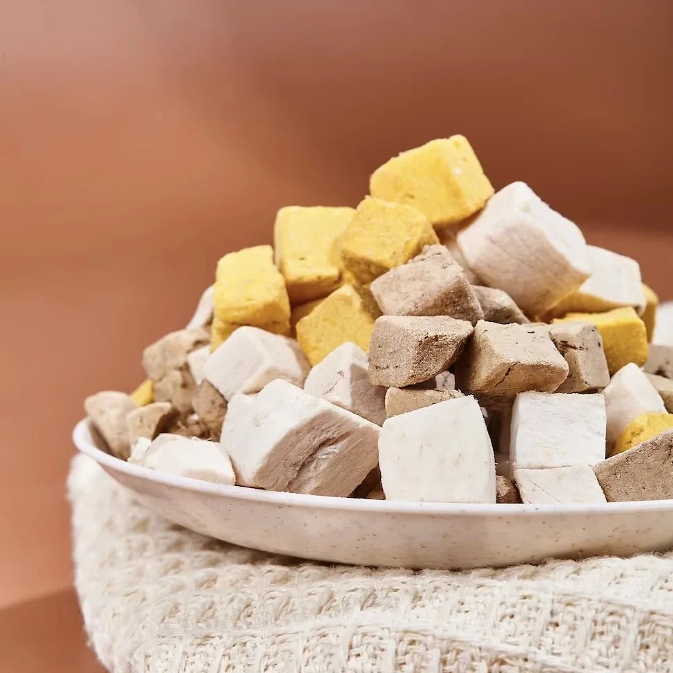 Assorted colored dog treats in a bowl on a textured surface with a blurred brown background