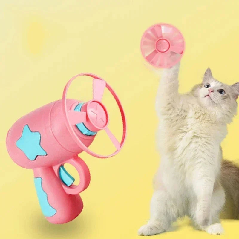 Pink and blue toy gun with a cat reaching for it on a yellow background
