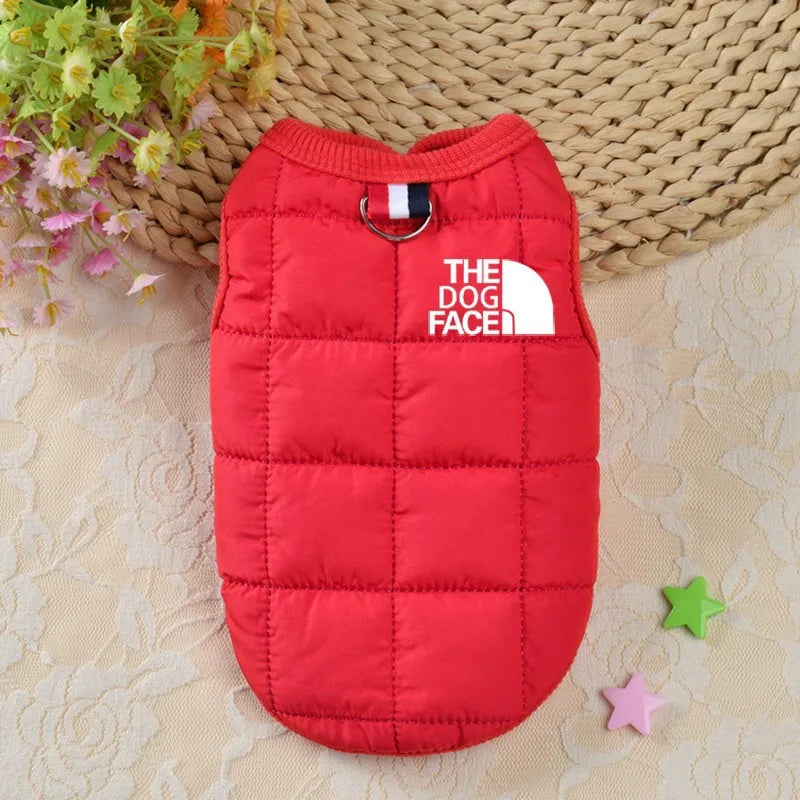 Red puffer vest for a dog with 'The Dog Face' logo on a textured surface.