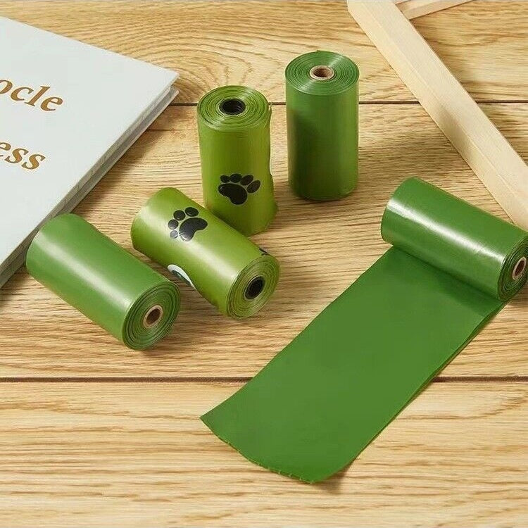 Green pet waste bags on a wooden surface with a book and wooden sticks.