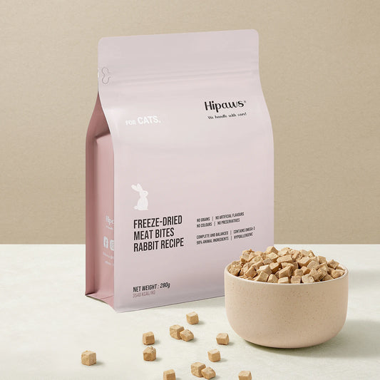 Pink package of Hipaws freeze-dried meat bites with a bowl of treats on a beige background