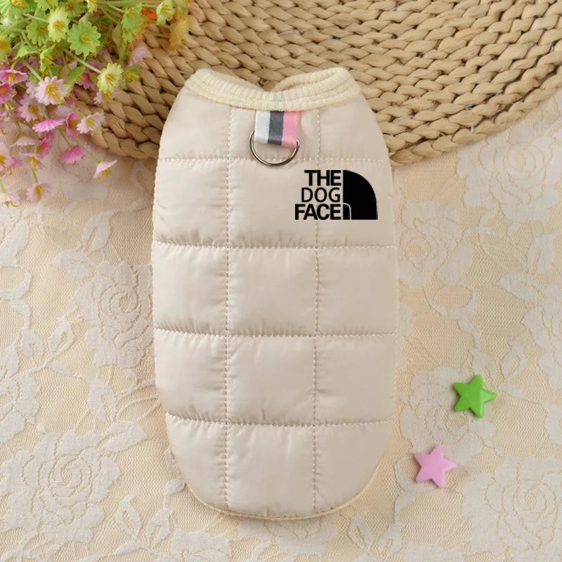 Beige quilted dog coat with 'The Dog Face' logo on a textured surface with flowers and stars.