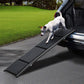 Dog using a black pet ramp to enter a vehicle on a driveway.