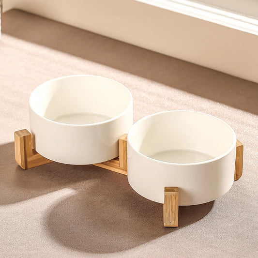 Two white ceramic bowls on a wooden stand on a beige carpet.