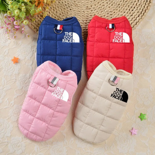 Four dog vests in blue, red, pink, and beige with 'The Dog Face' logo on a textured surface.