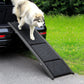 Dog using a black pet ramp to get into a car on a grassy area.