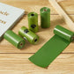 Green pet waste bags on a wooden surface with a book and wooden sticks.