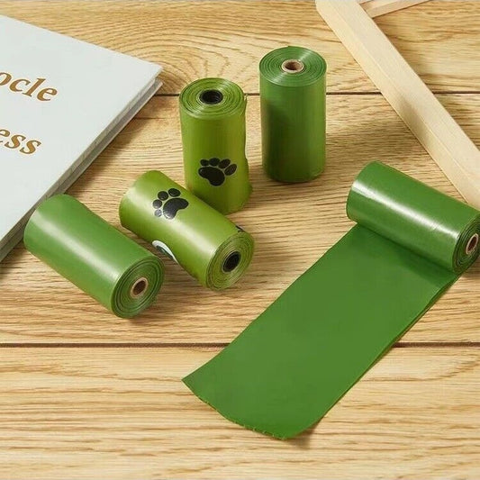 Green pet waste bags on a wooden surface with a book and wooden sticks.
